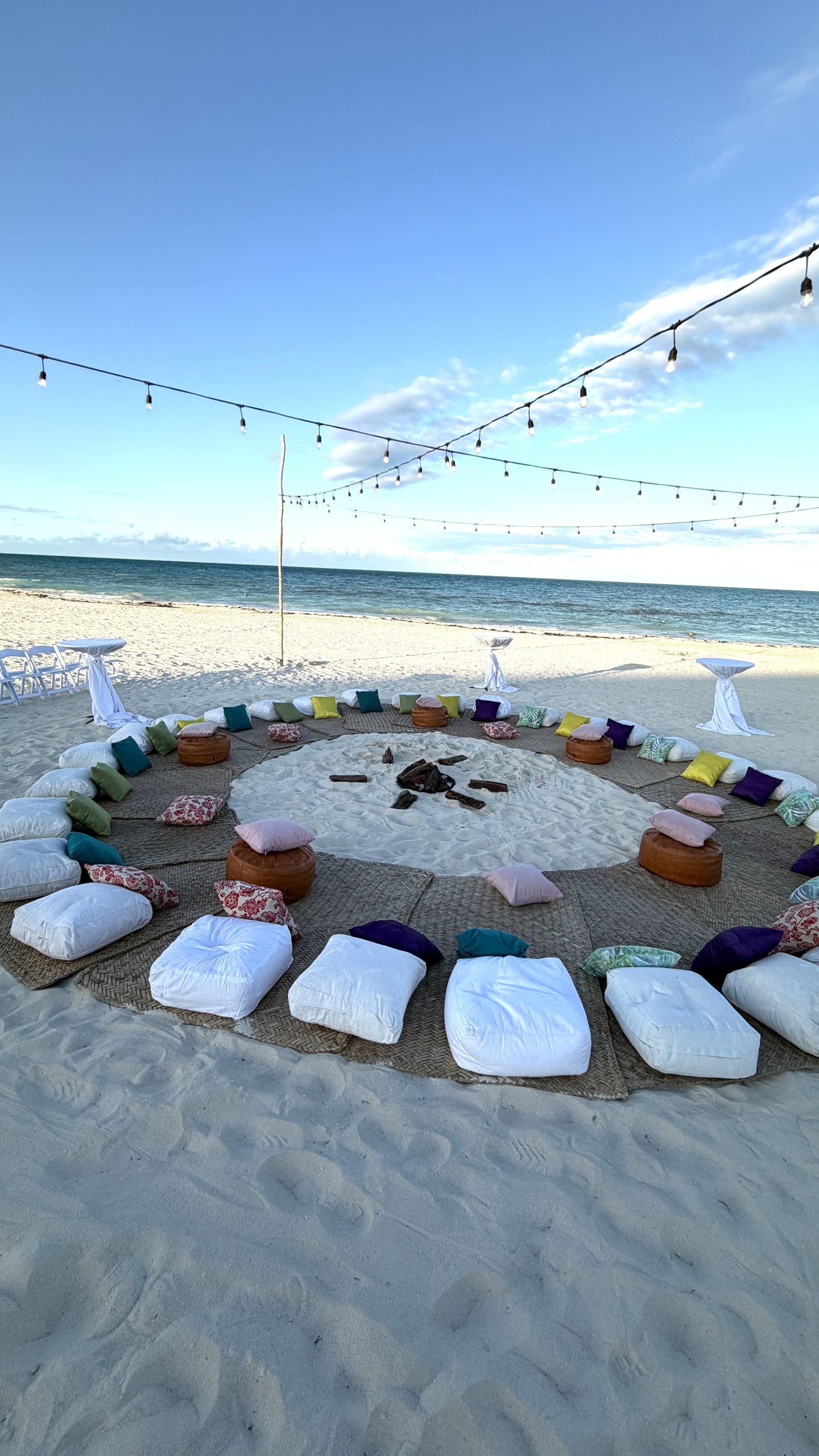 Beach bonfire setup with string lights and floor cushions for destination wedding welcome party in Mexico